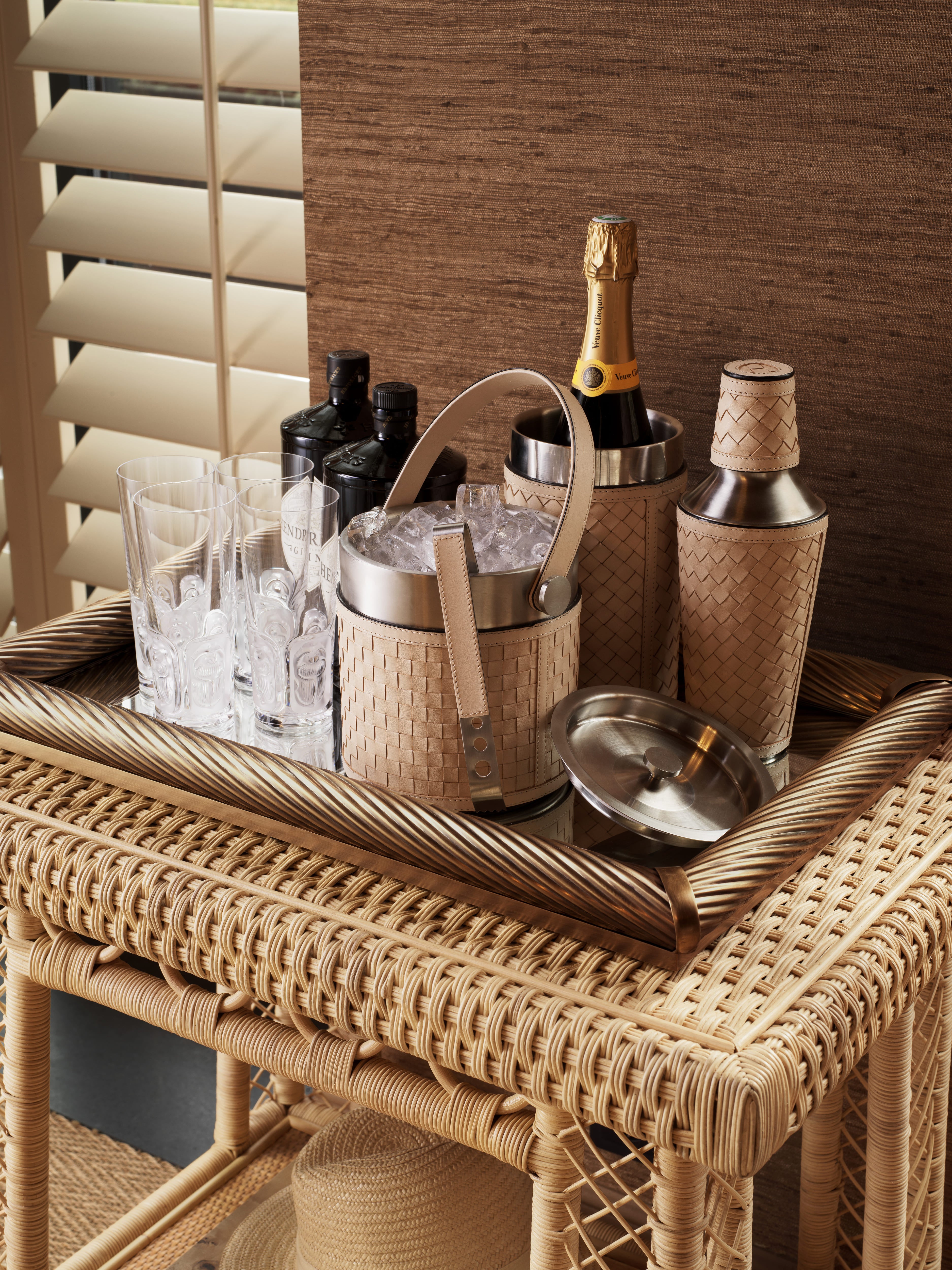 Elegantes Eichholtz Bar-Set mit Champagnerkühler, Gläsern und geflochtenen Wohnaccessoires auf Rattanwagen.